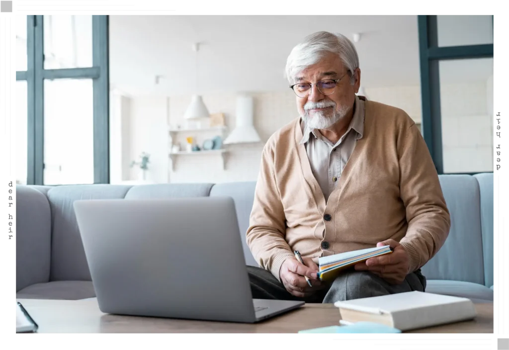An older man sitting comfortably on his sofa at home, holding a notebook and pen while looking attentively at his laptop — reflecting a calm, self-paced online session guided from the comfort of home.